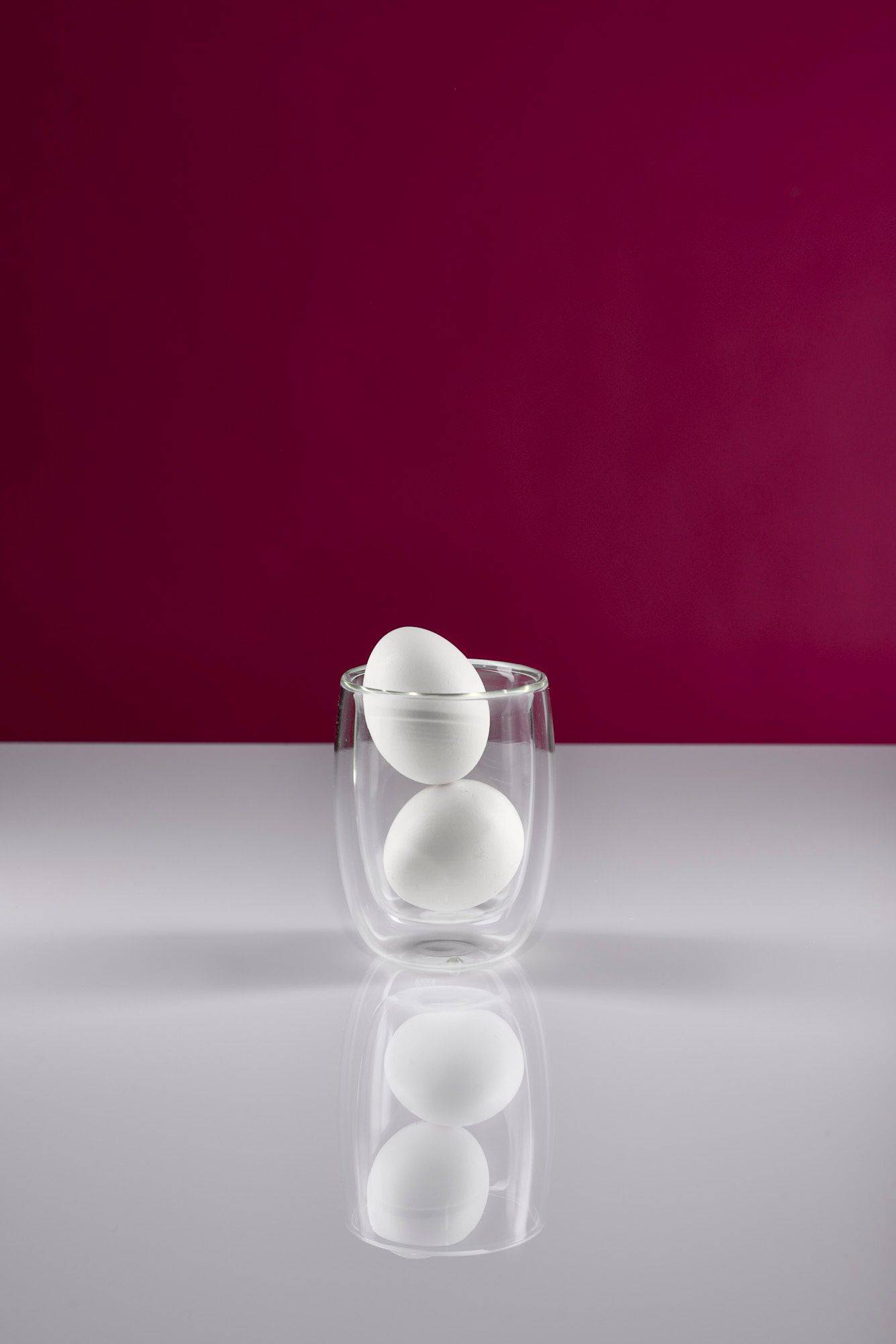 two white eggs in a glass with white and pink background