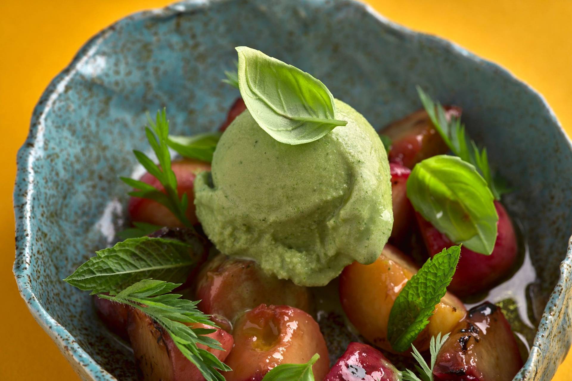 herbs and yogurt ice cream with grilled peaches and greek olive oil in a turquoise ceramic bowl with yellow background