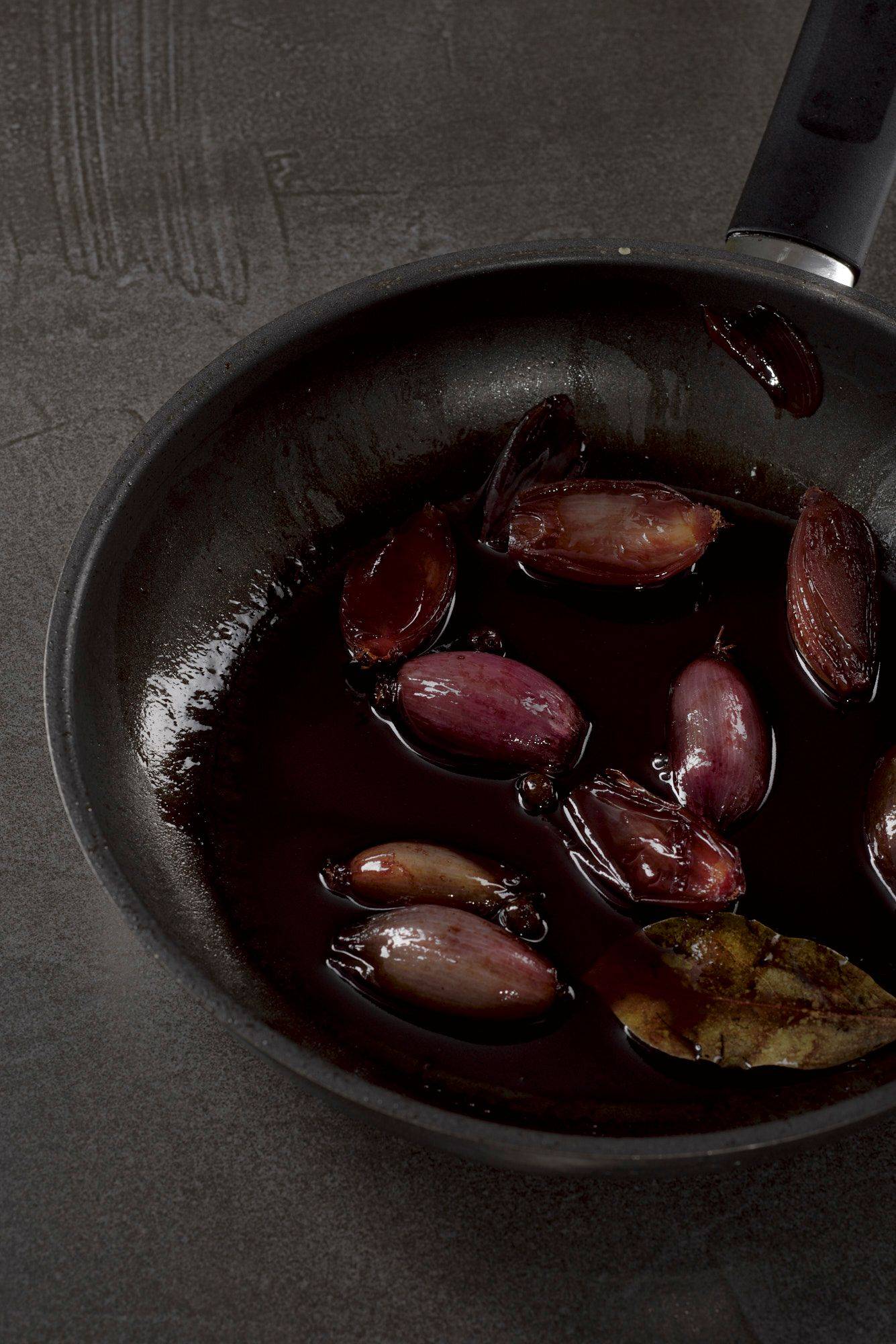 red wine shallots in a pan on a gray sapienstone top with green background