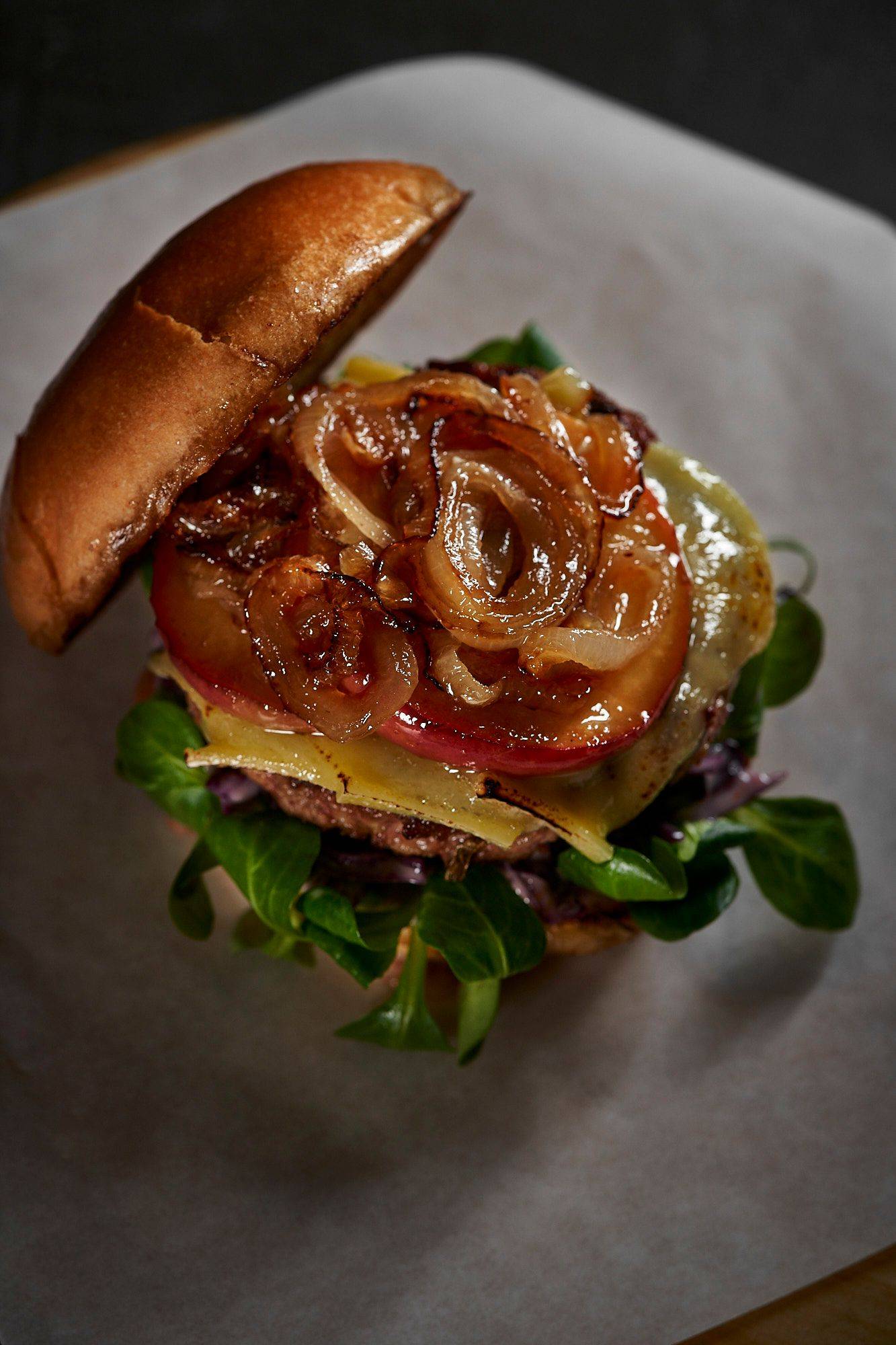 goose burger with red cabbage coleslaw raclette cheese and caramelized apple on a wooden board