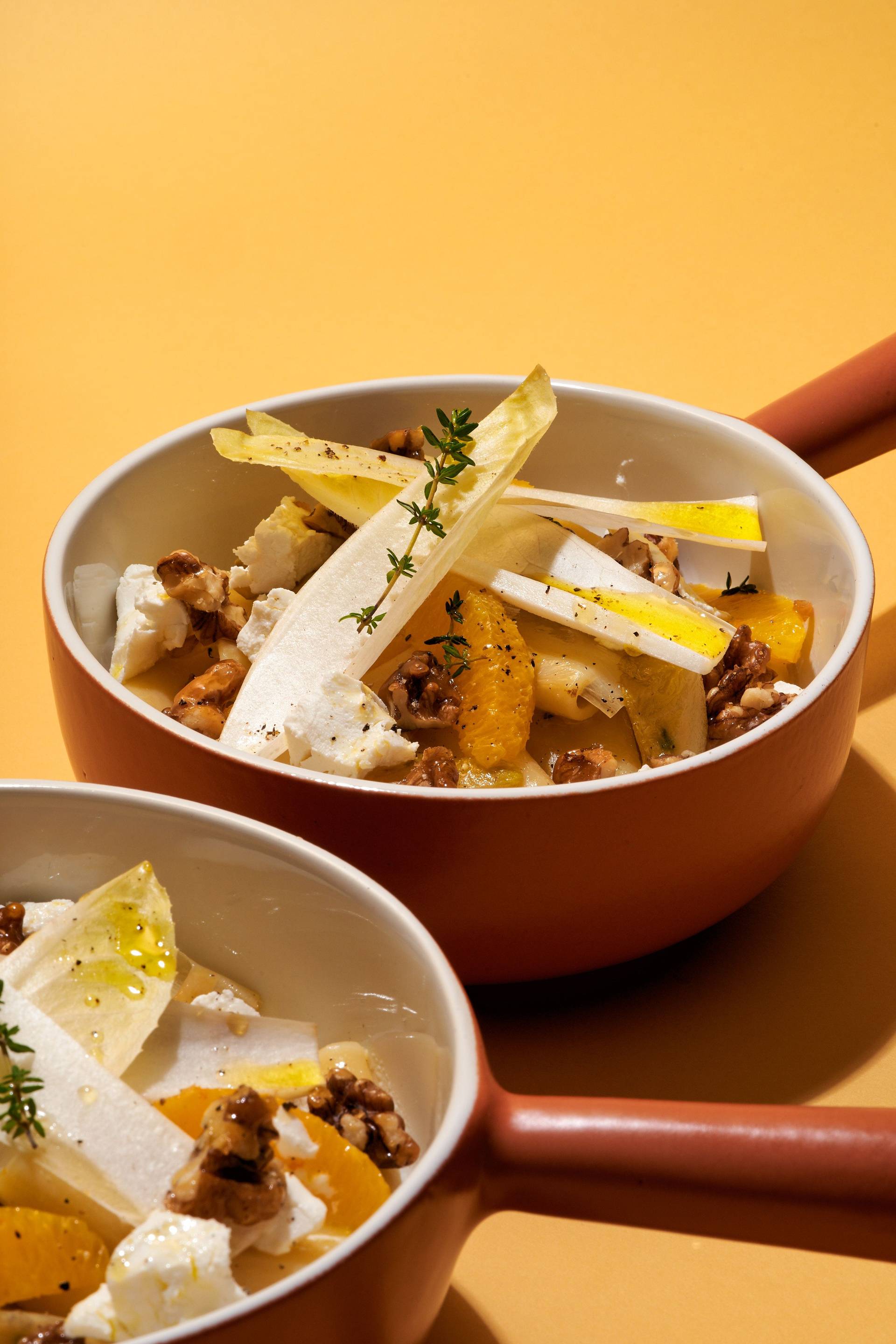 two bowls of vegetarian one pot pasta with chicory, orange, goat cheese and candied walnuts on yellow background