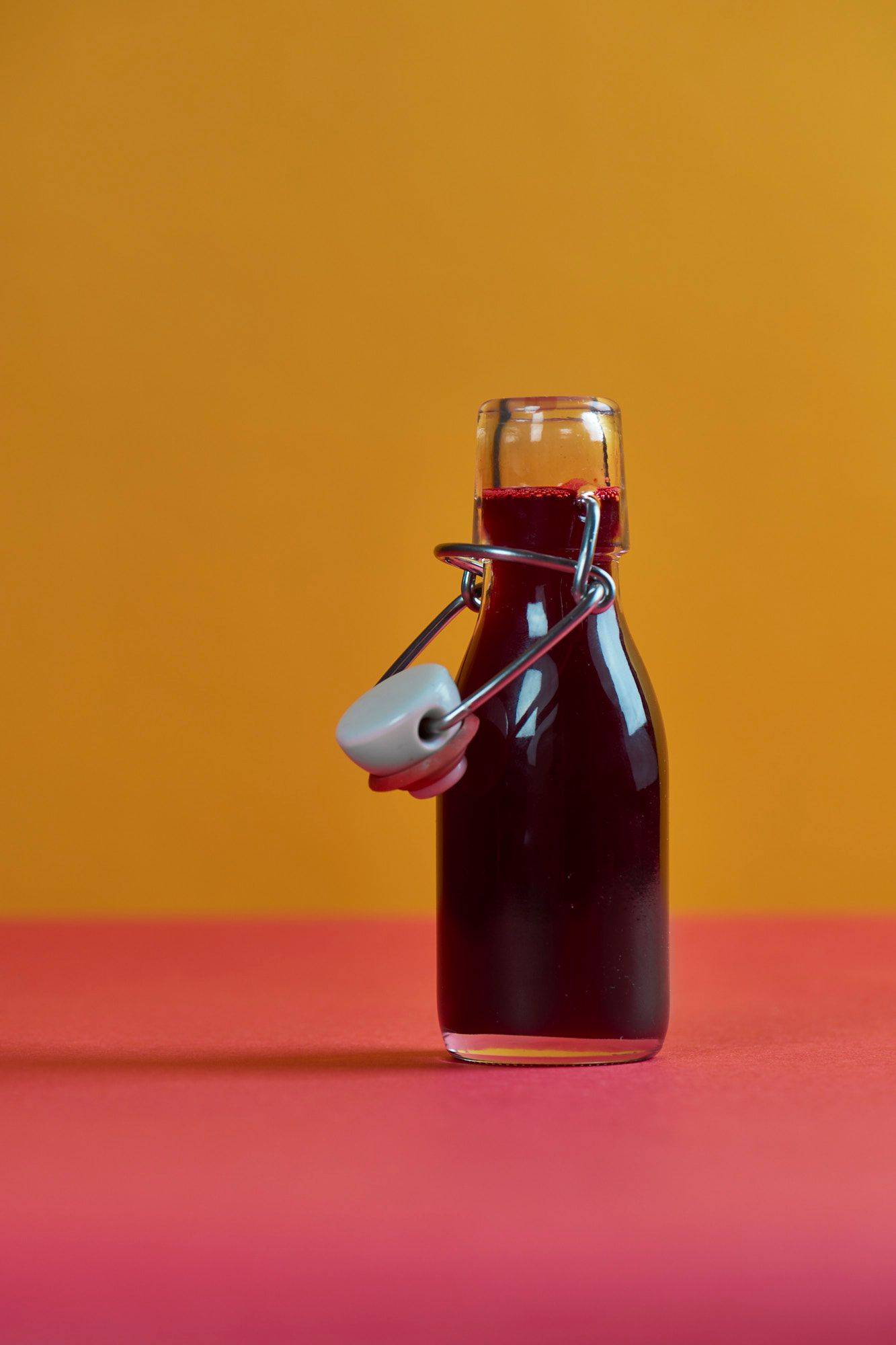 eine kleine flasche rote beete saft mit rotem und gelbem hintergrund