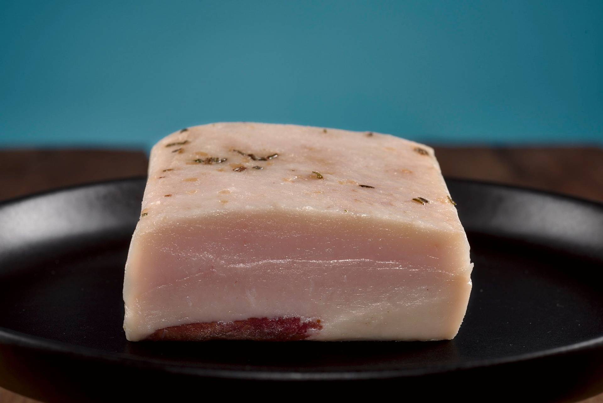 organic german lardo bacon on a black plate with wooden table and blue background