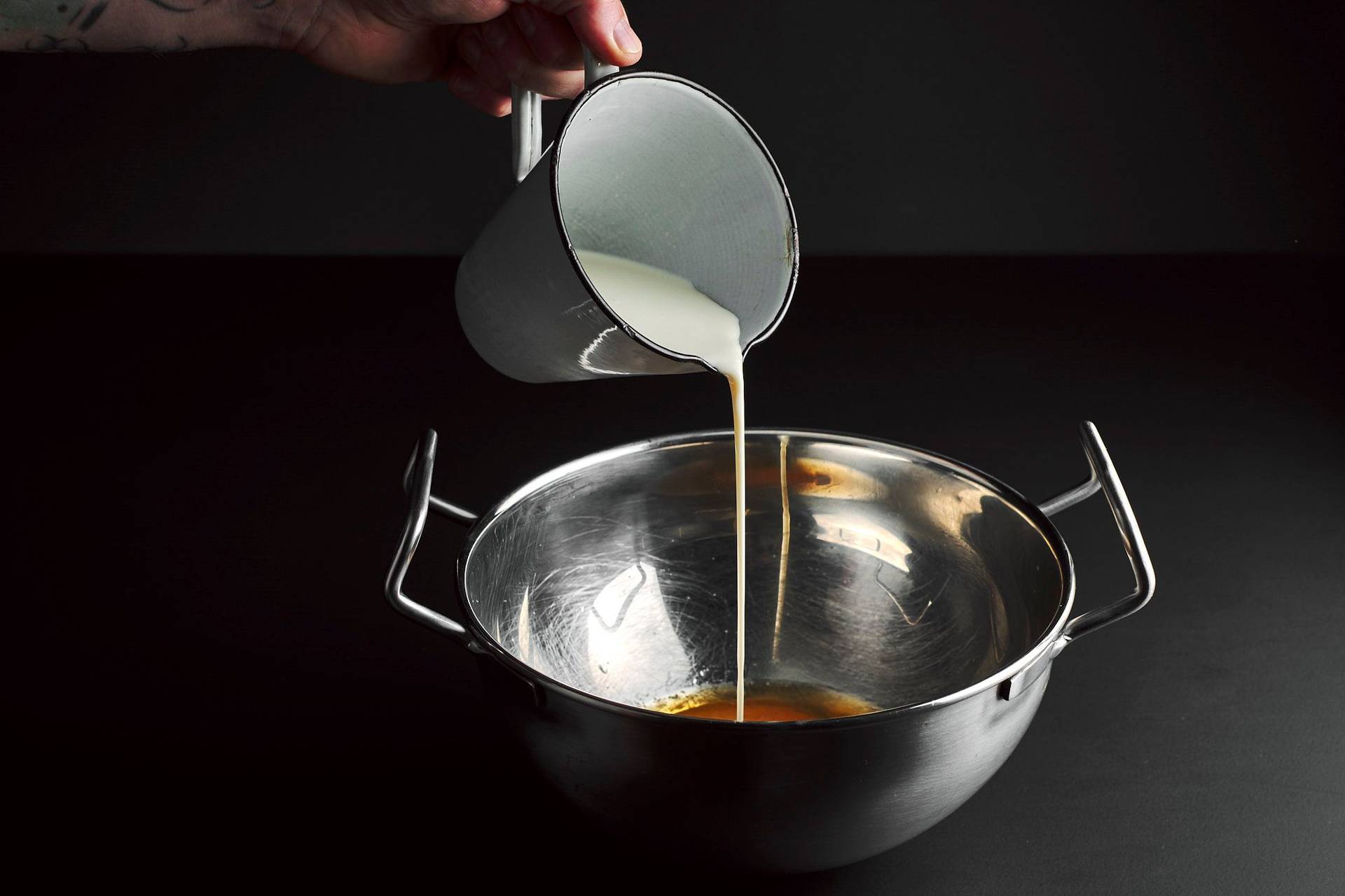 pouring condensed milk into a bowl with egg yolks with black background