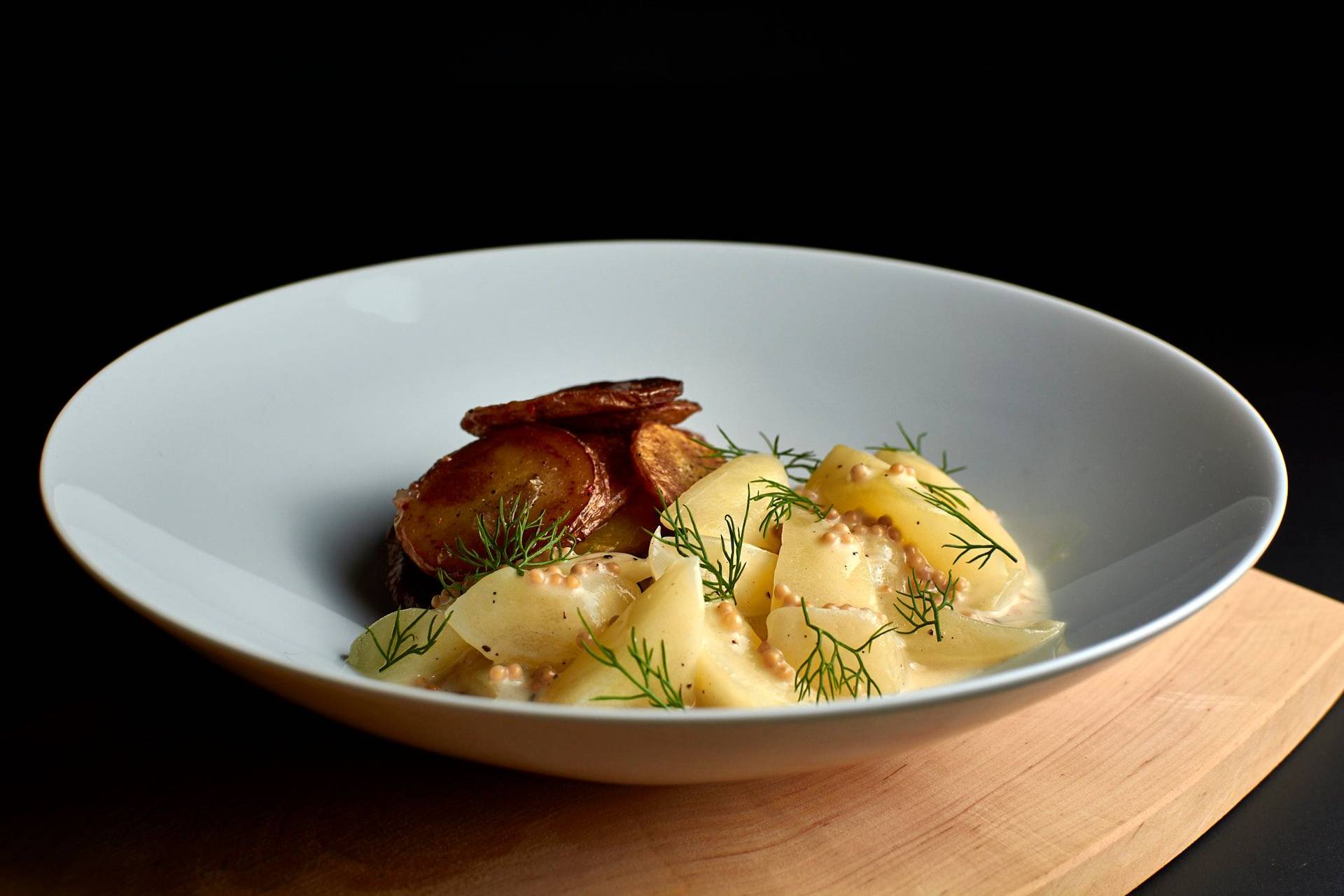 braised cucumbers with roasted potatoes in a white bowl on black background