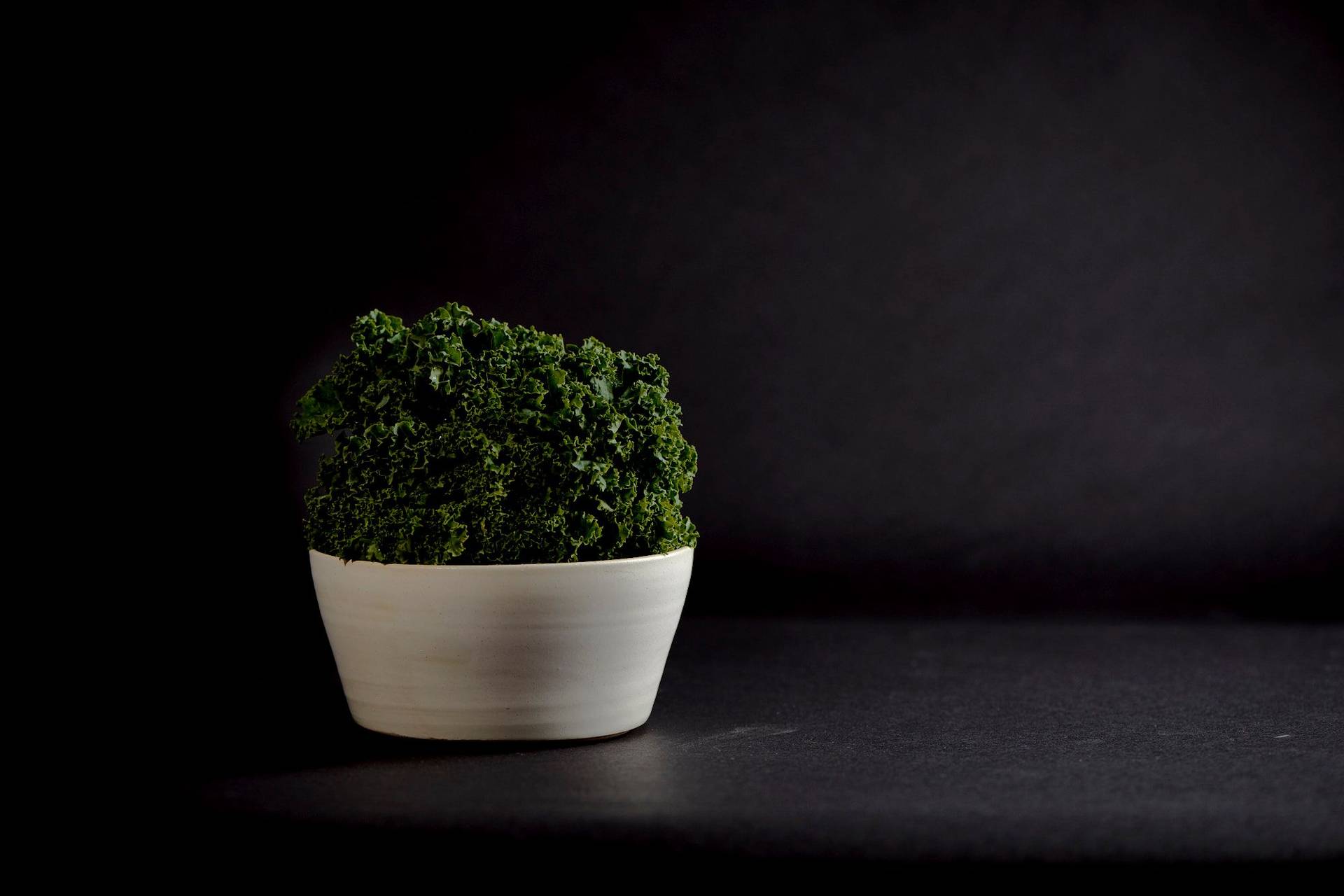 a ceramic bowl with kale with black background