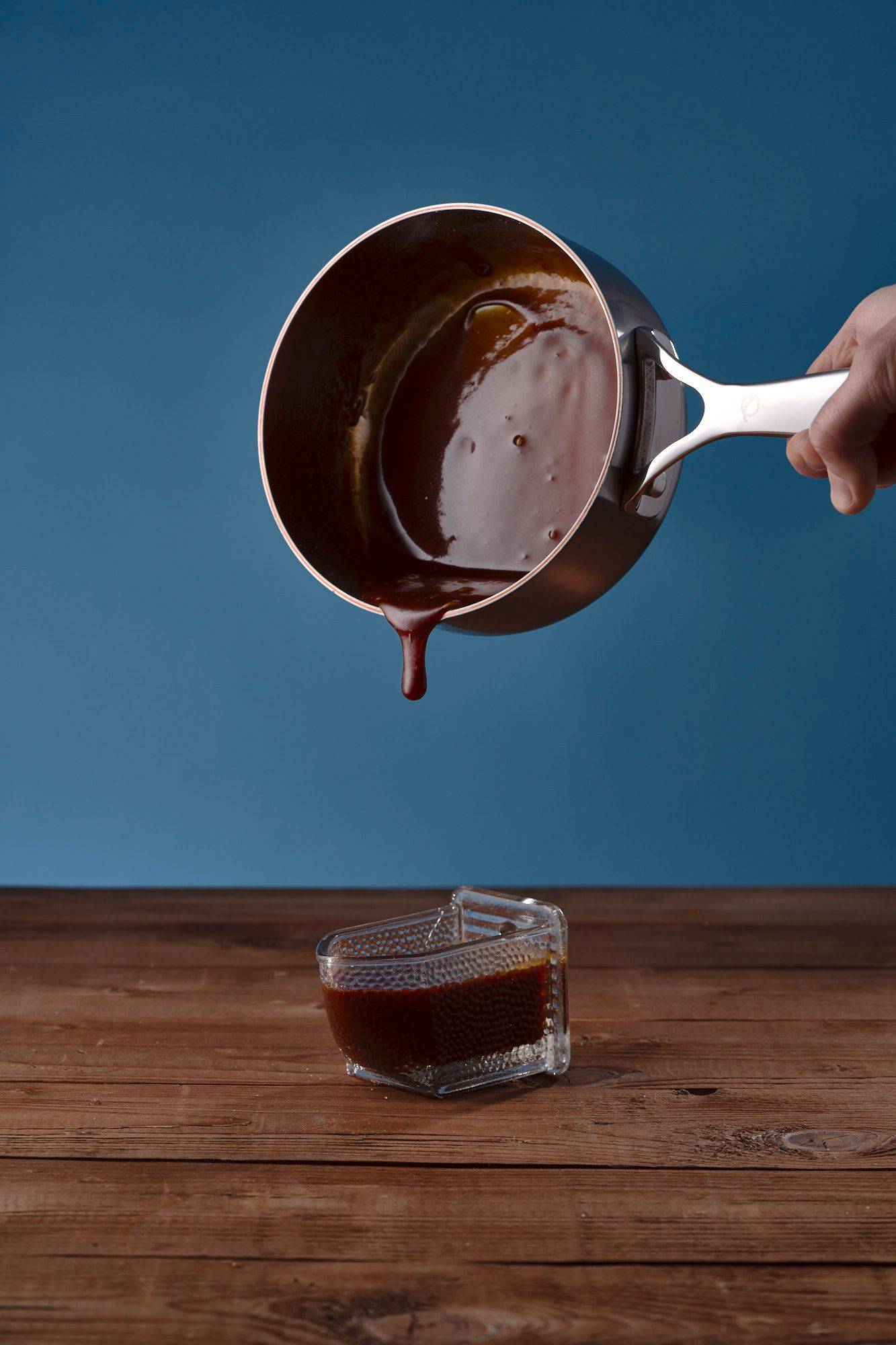 pouring salted caramel into vintage jar on a wooden table with blue background