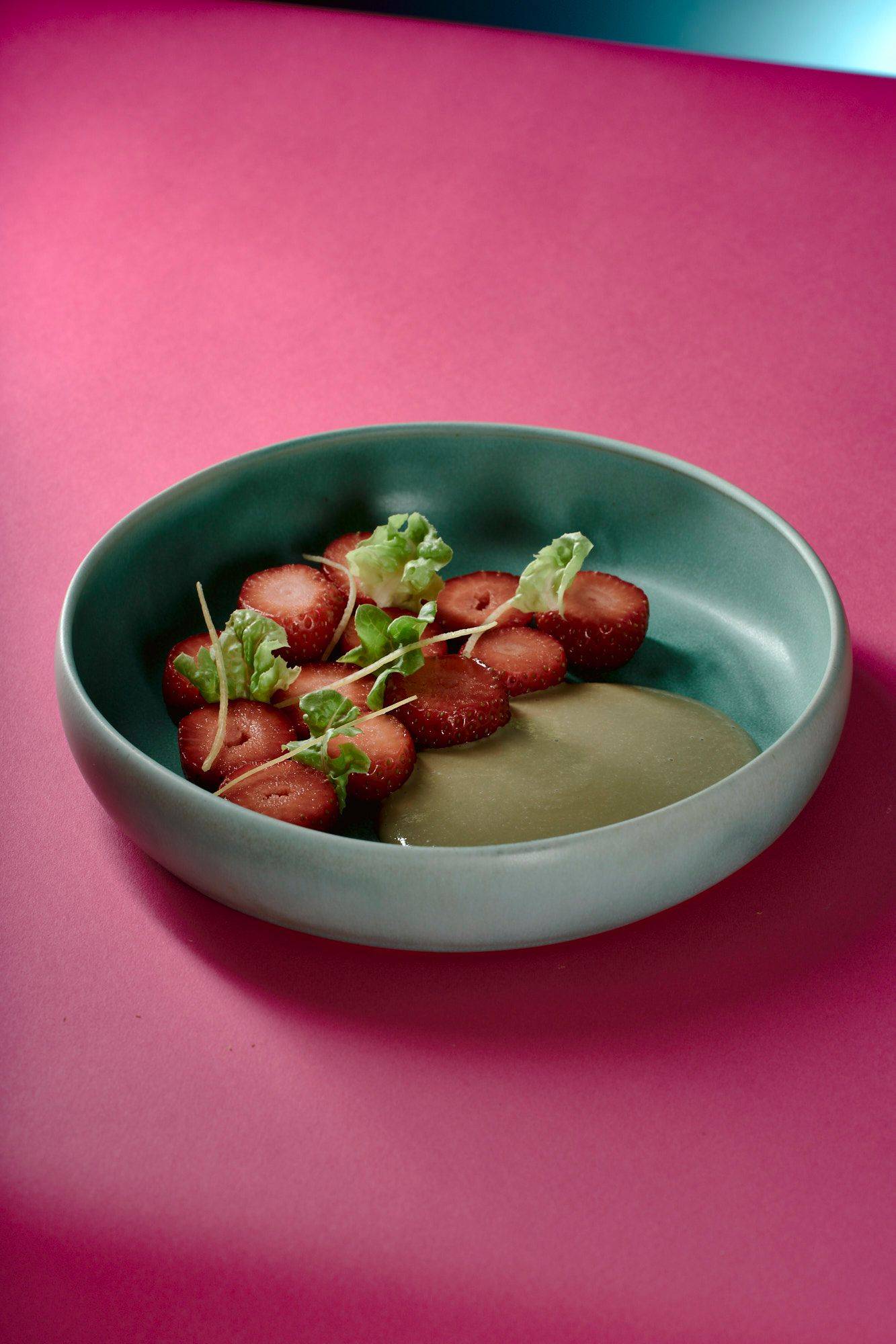 vegan strawberry dessert with lettuce and sunflower seeds on a turquoise plate with pink background