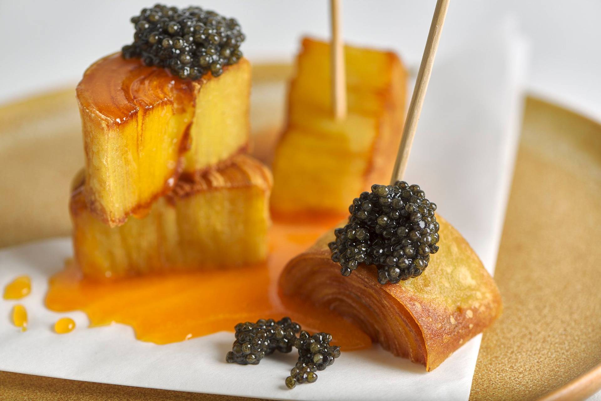 crispy potato swirls with egg yolk and caviar on a brown ceramic plate with white background