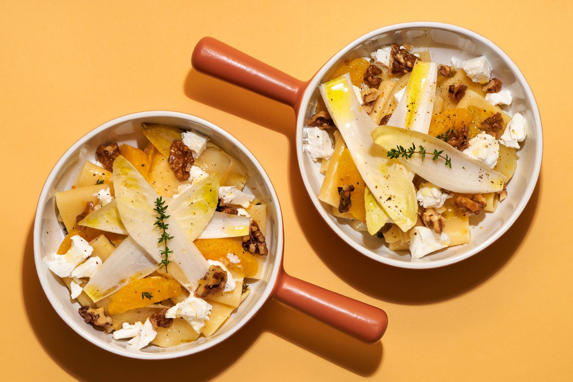 top shot of two bowls of vegetarian one pot pasta with chicory, orange, goat cheese and candied walnuts on yellow background