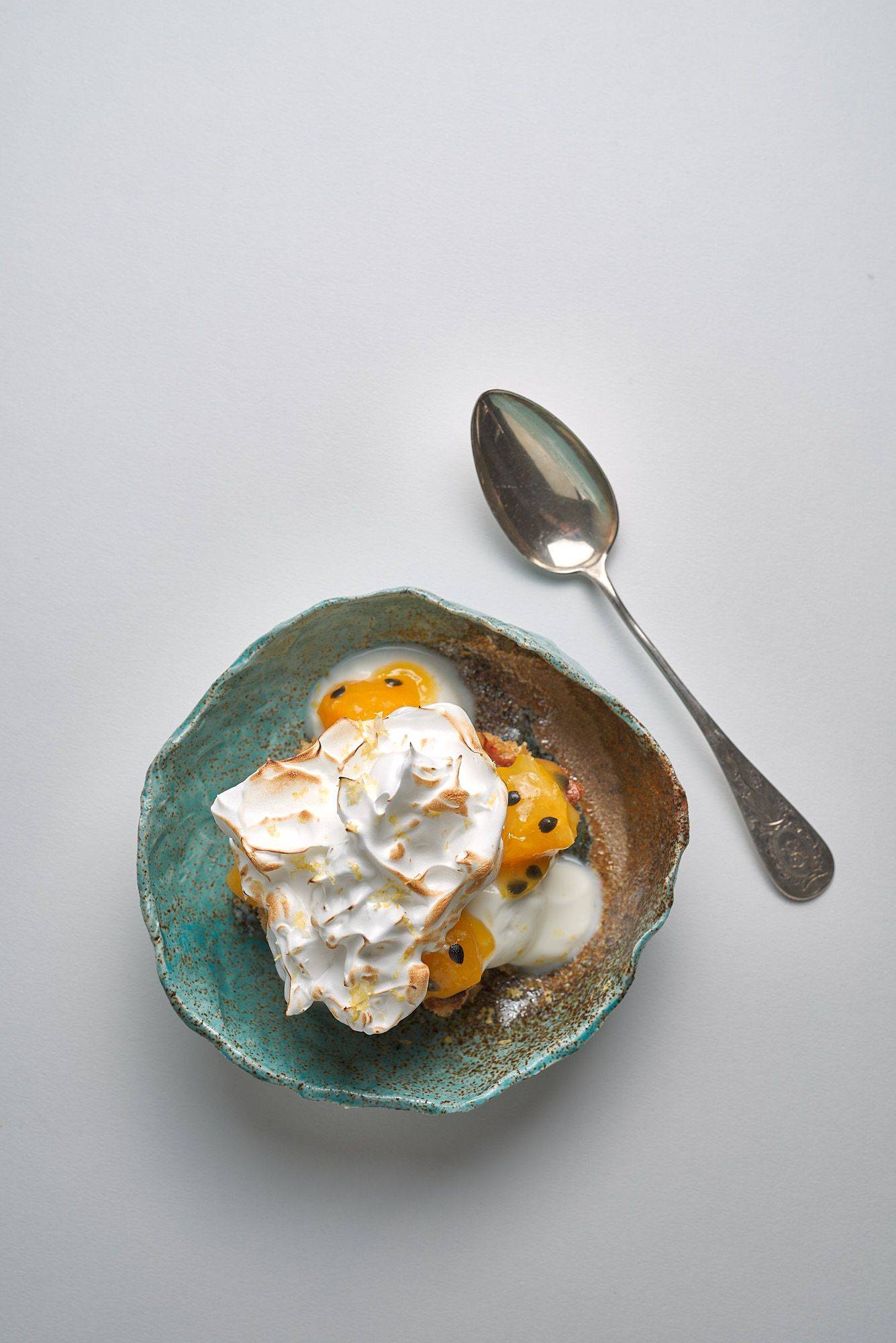 Passionsfrucht Baiser Dessert in blauer Keramikschale vor weißem Hintergrund