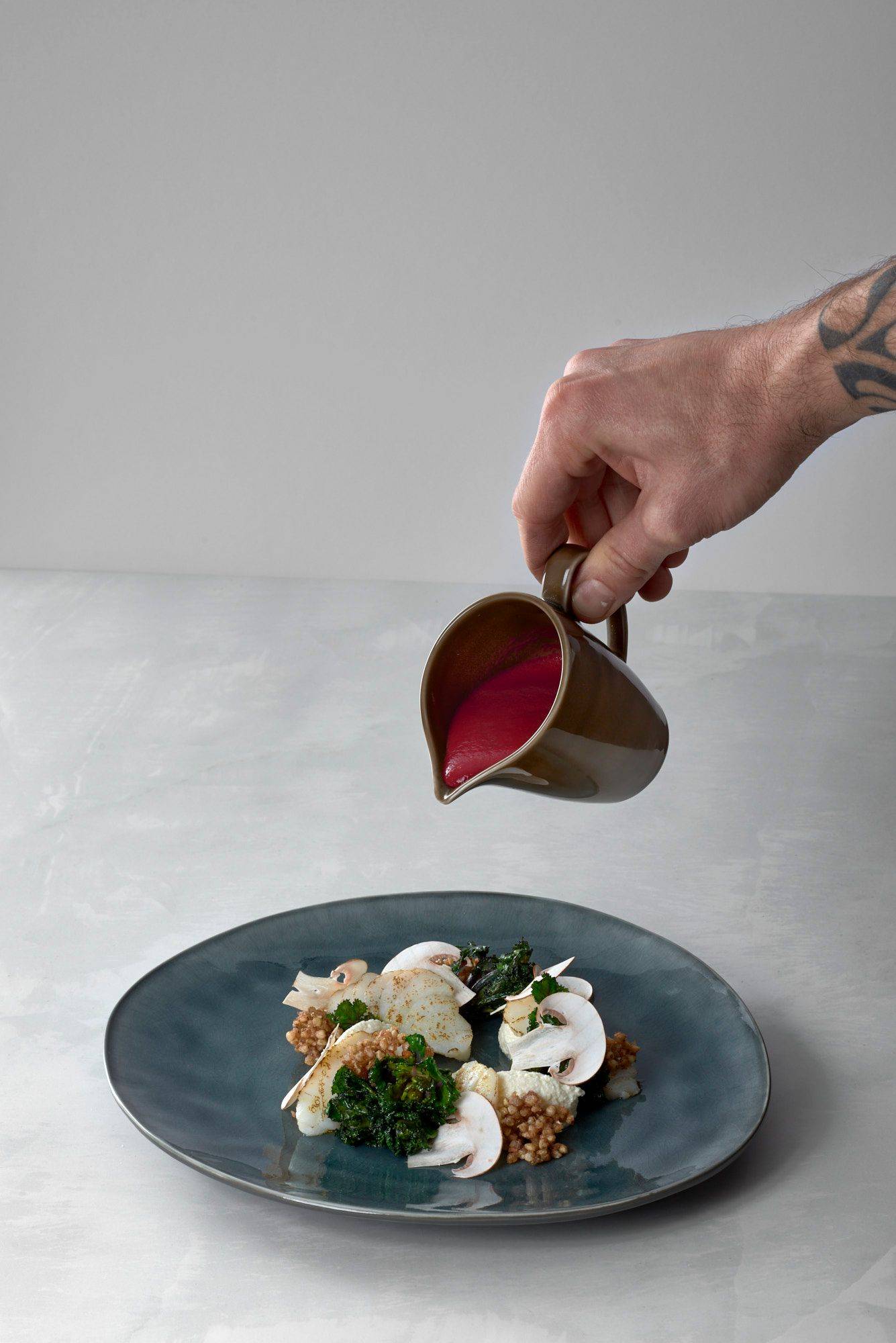 kabeljau mit roter beete ricotta molke und buchweizenpops auf einem grauen teller mit weißem sapienstone top