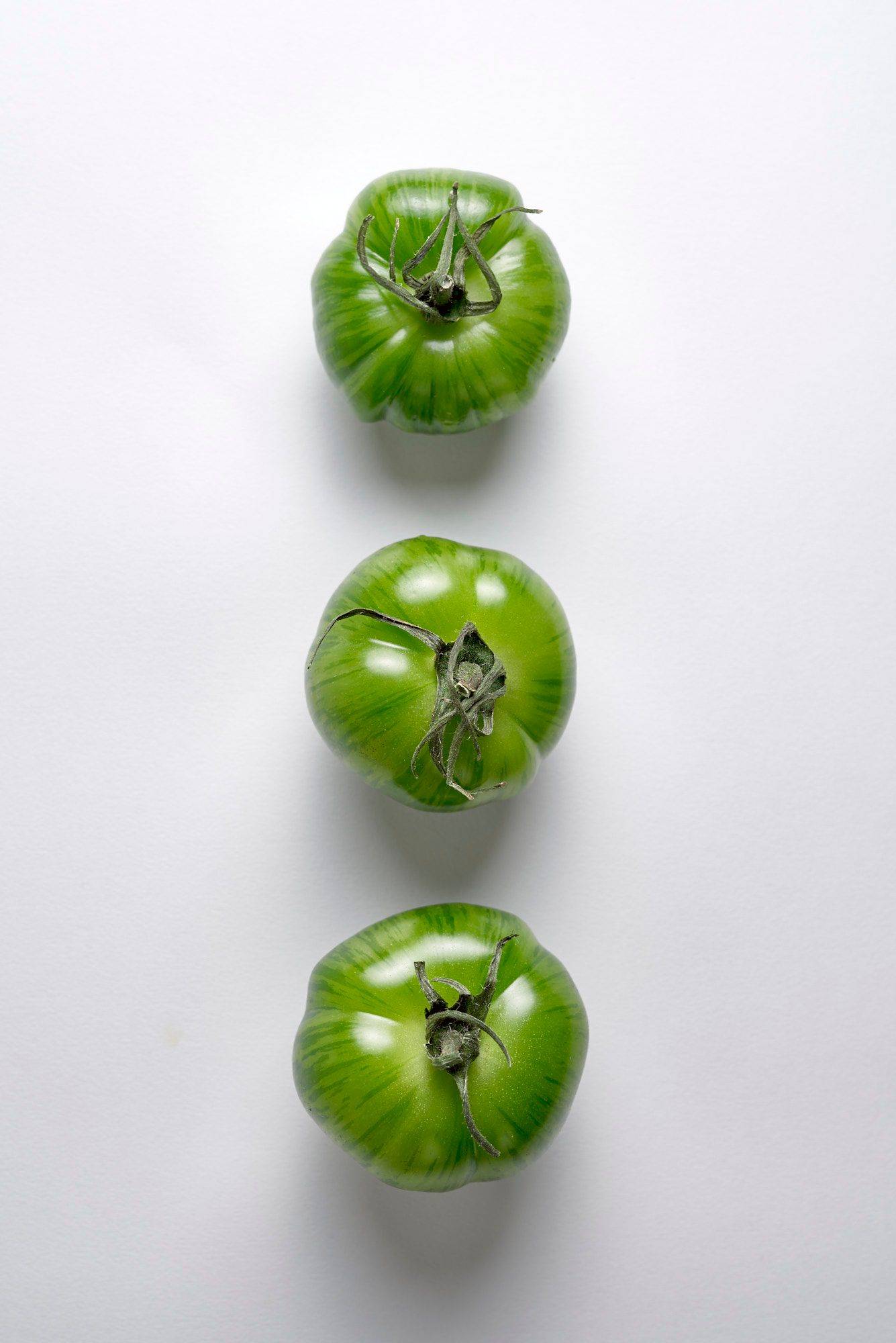 three green tomatoes on white background
