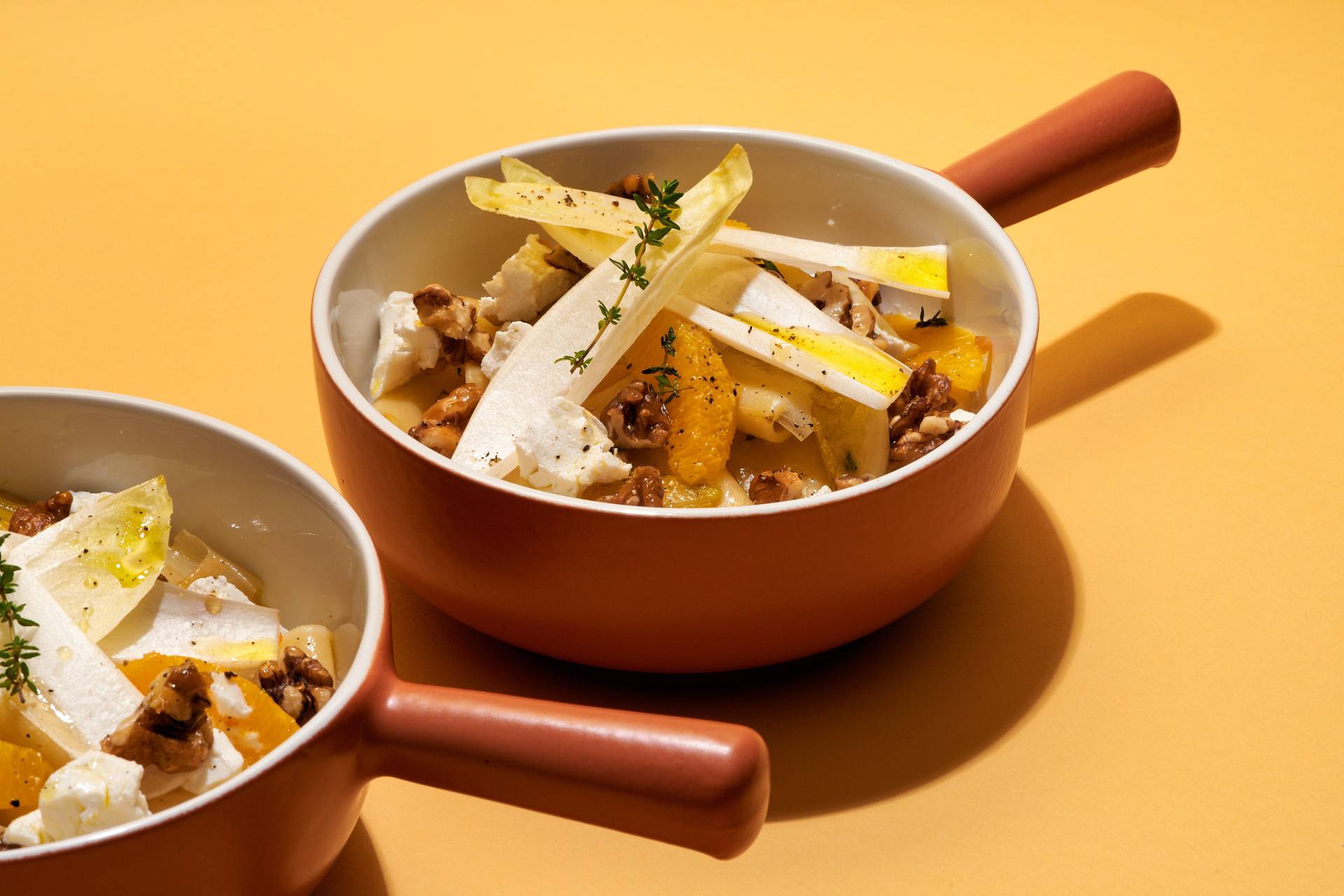 two bowls of vegetarian one pot pasta with chicory, orange, goat cheese and candied walnuts on yellow background