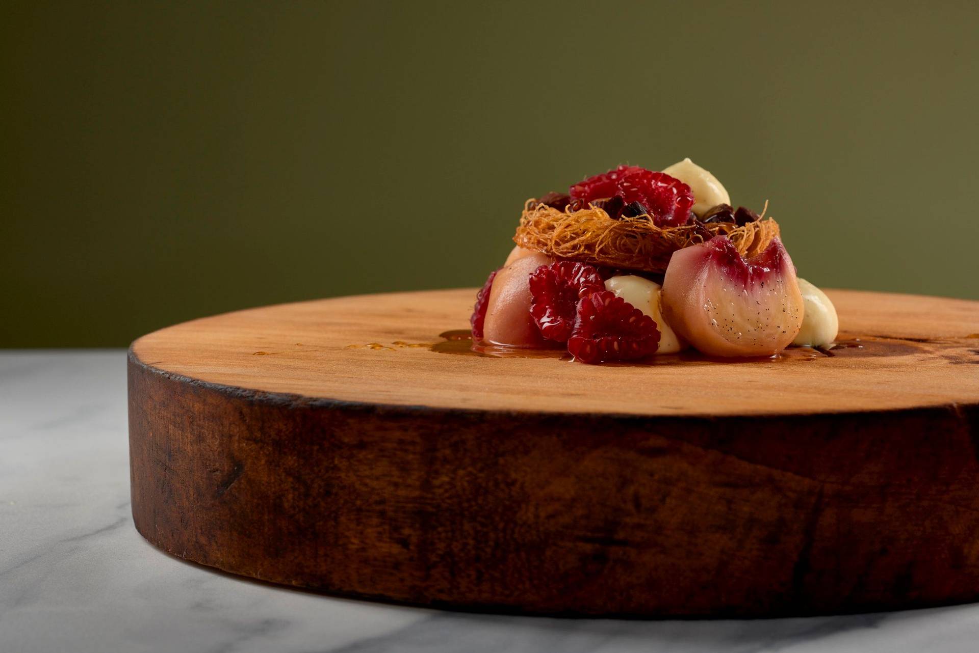 peach melba dessert on a wooden plate with a marbled sapienstone top and green background