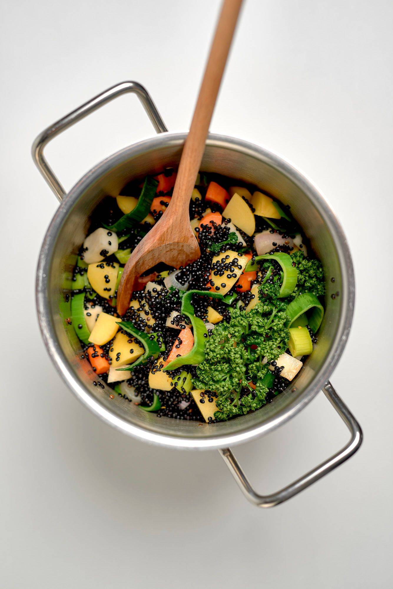 making black beluga lentil soup in a silver pot on white background