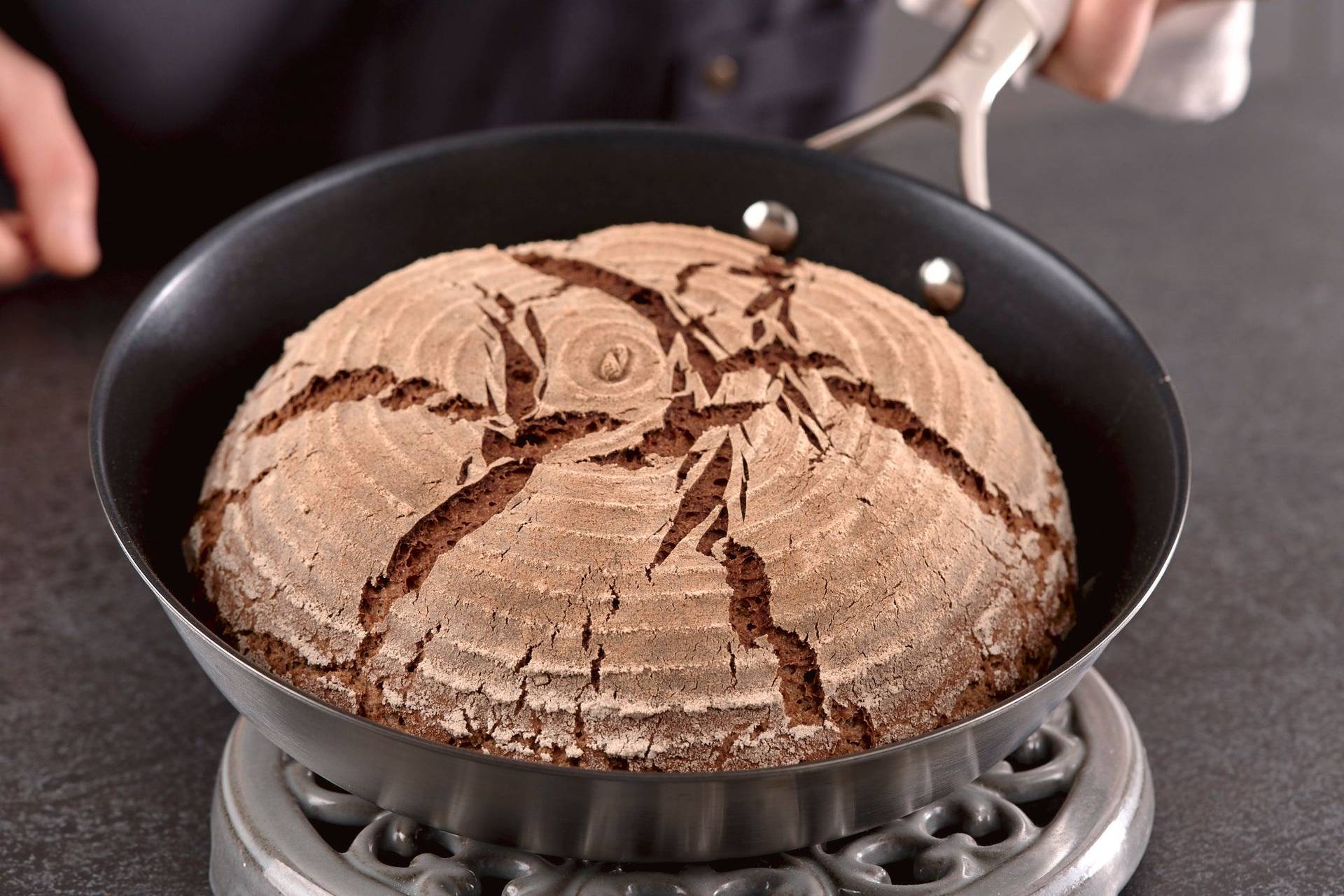 mann hält in der pfanne gebackenes roggen sauerteigbrot in heimischer küche