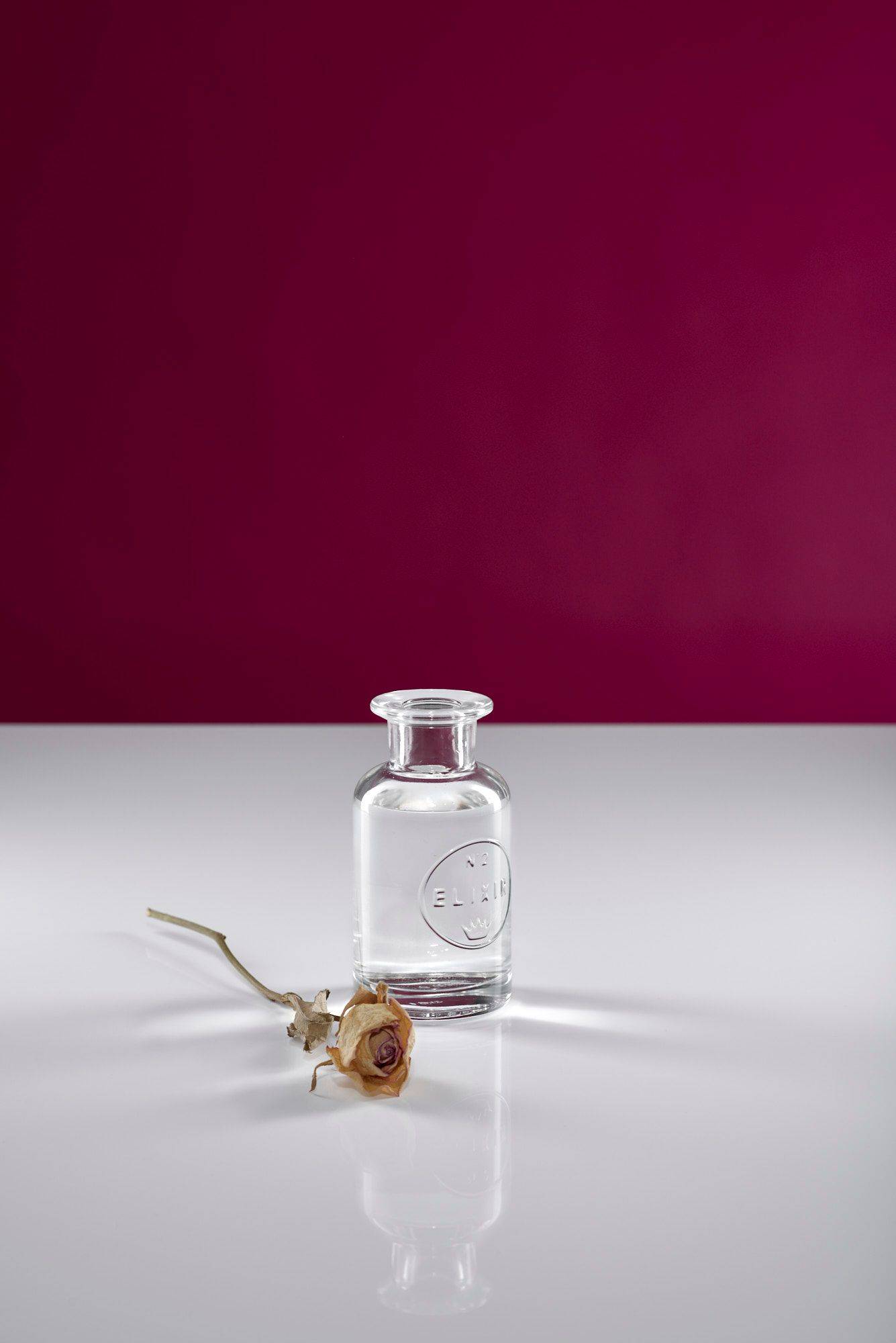 a glass bottle of rose water with white and pink background