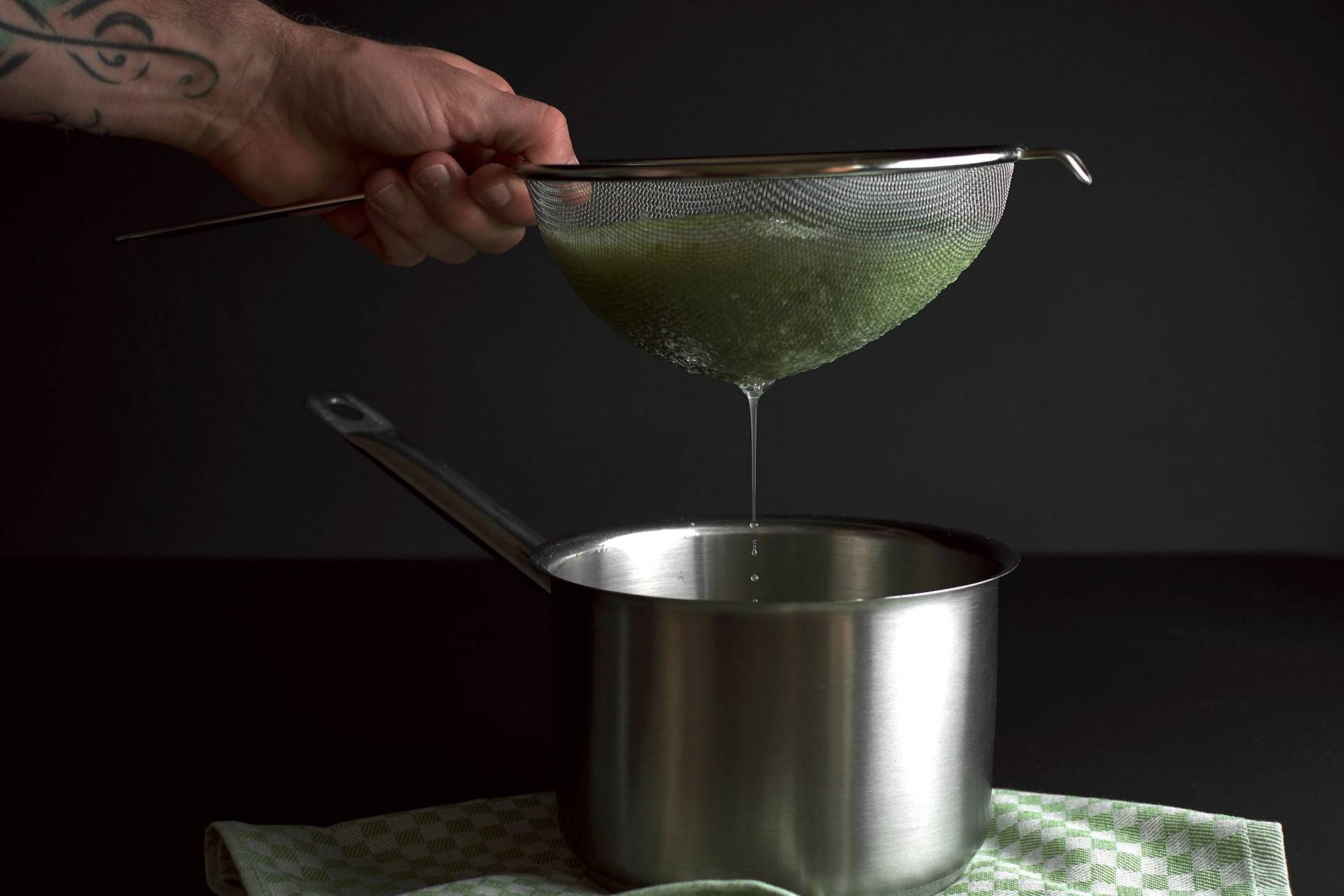 straining cucumber lemonade on black background