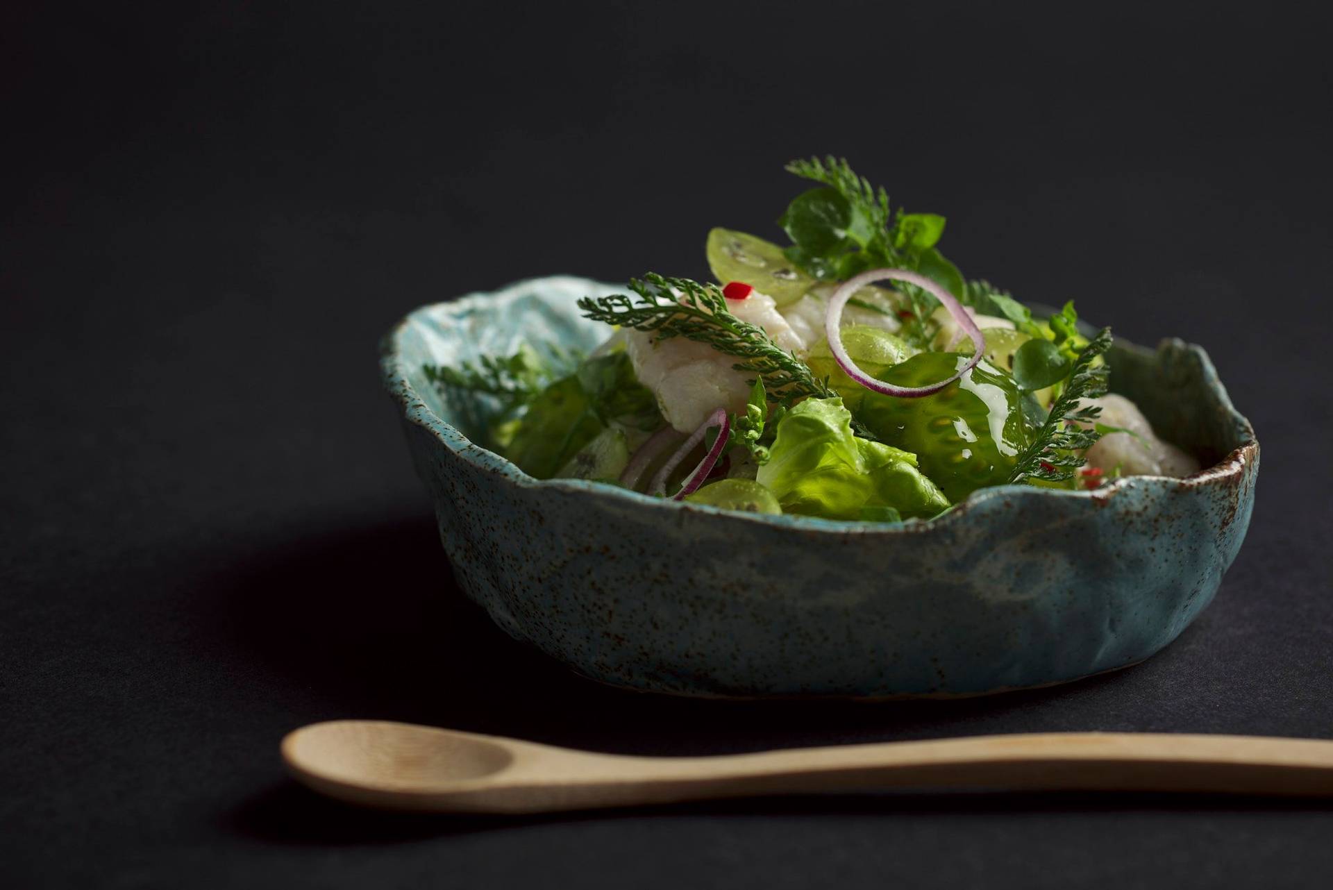 cod ceviche with gooseberries in a turquoise ceramic bowl with black background